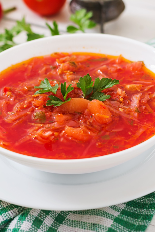 Горячий борщ с зеленью в белой тарелке на столе