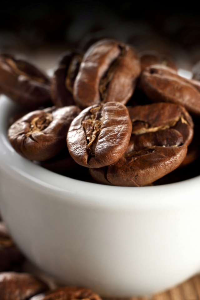 Много кофейных зерен в белой чашке на столе