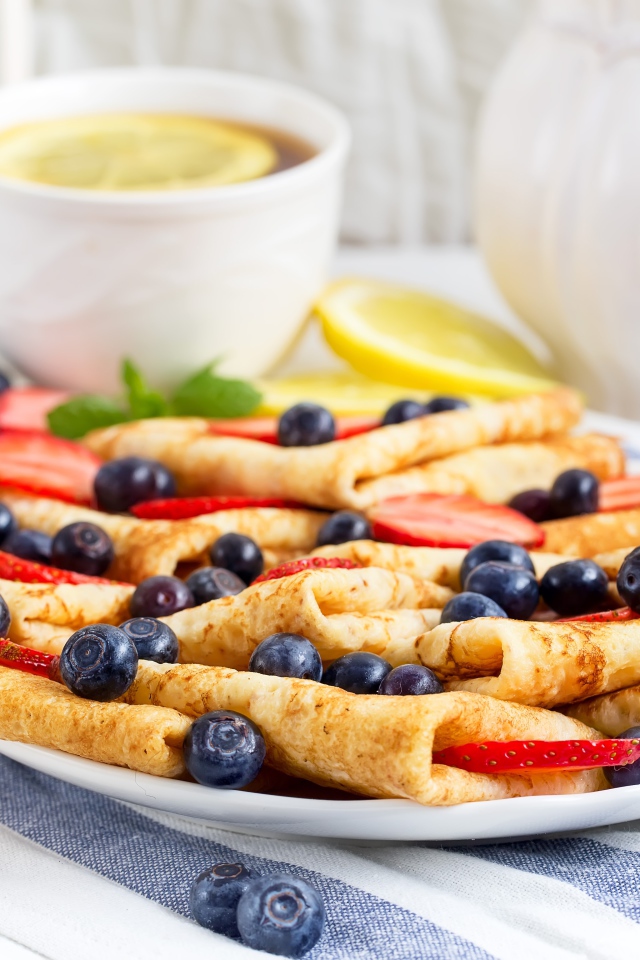 Блины с ягодами черники и клубники на столе с чашкой чаю