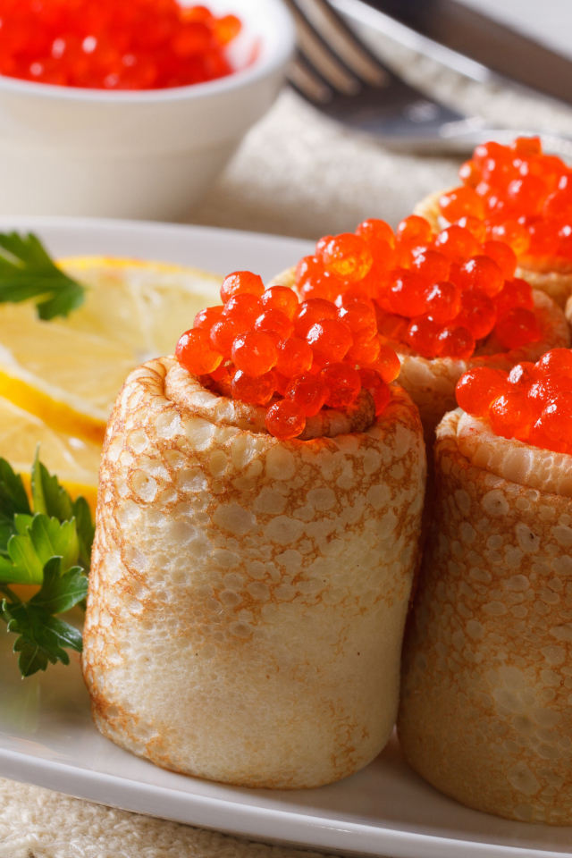 Блины с красной икрой на тарелке с лимонами и петрушкой