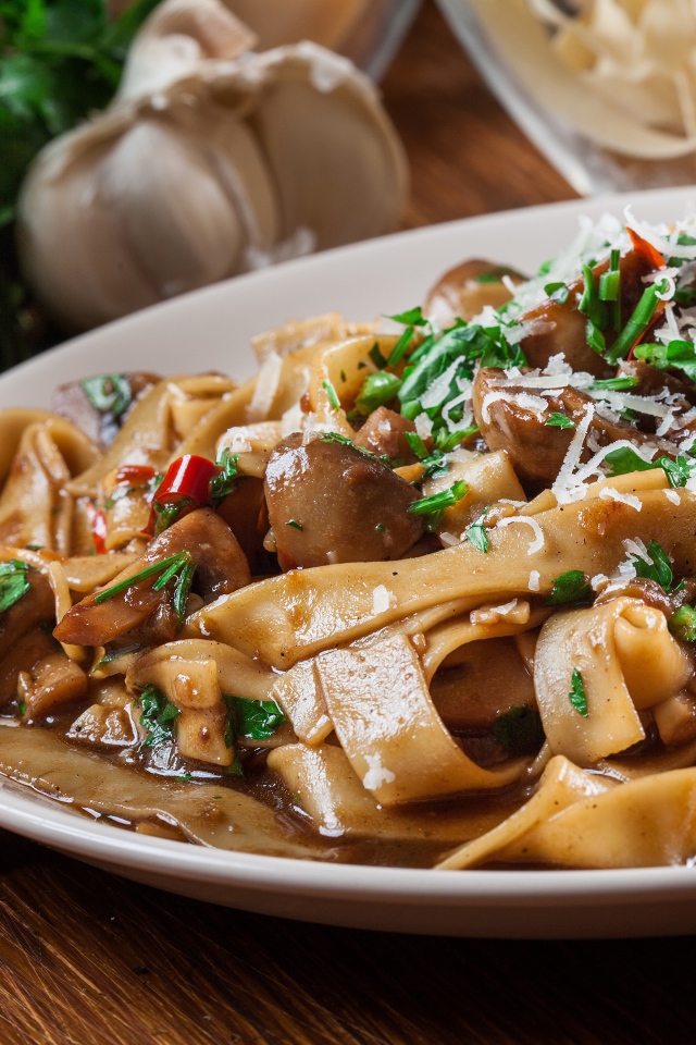 Паста с грибами, сыром и  зеленью на столе с чесноком 