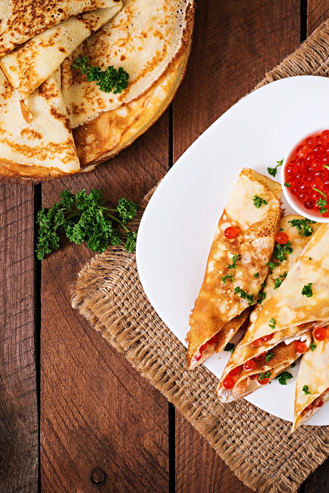 Рулетики из блинов на белой тарелке с красной икрой 