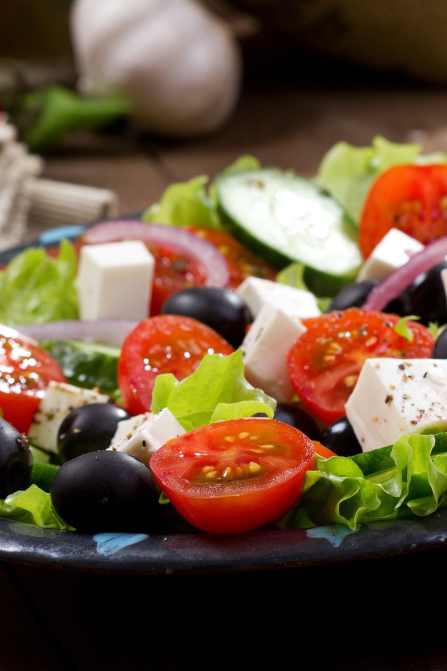 Салат с помидорами, огурцами, оливками, кусочками сыра и луком на листьях салата