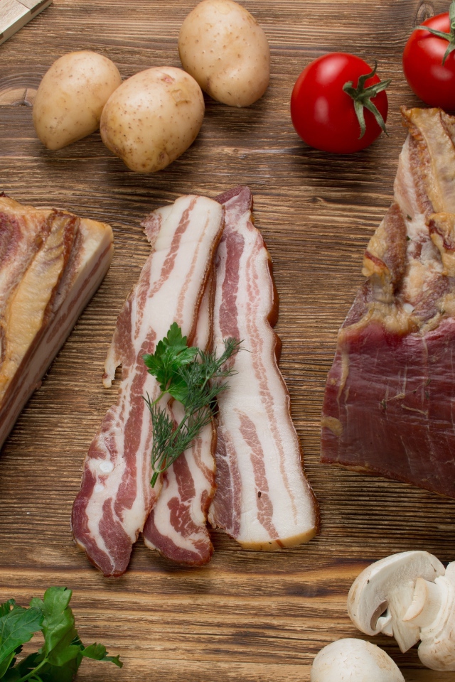Нарезанное сало на столе с картофелем, помидорами и грибами 