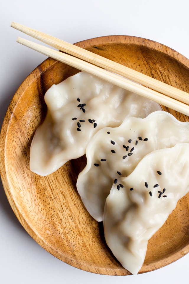 Три вареника на деревянной тарелке с палочками