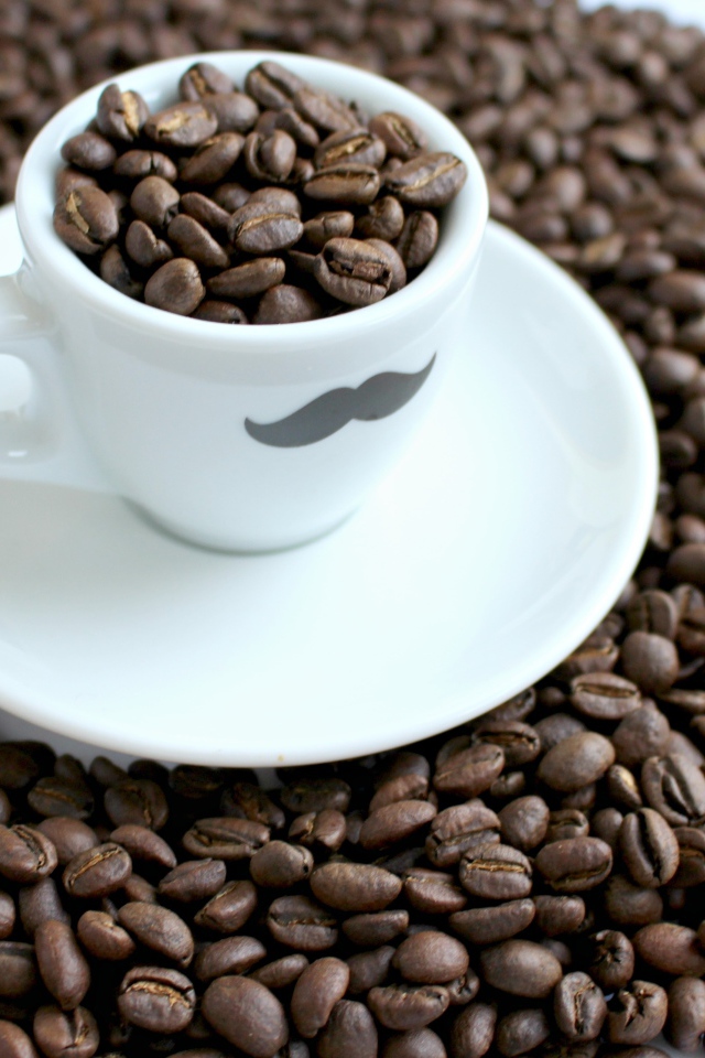 Белая чашка с жареными кофейными зернами стоит на столе с кофейными зернами