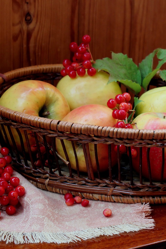 Красивые яблоки в корзине на столе с ягодами калины