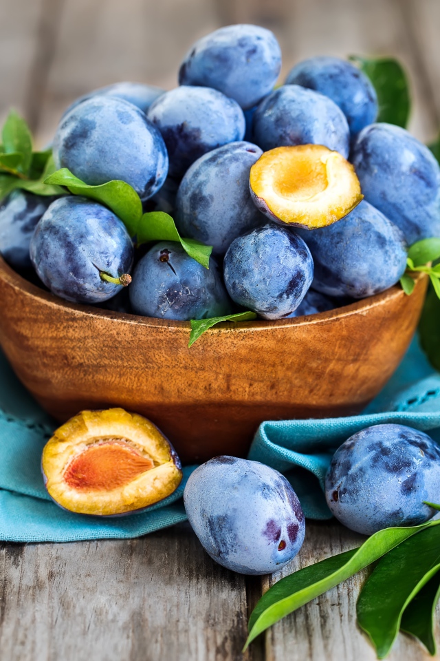 Синие сливы в деревянной миске с зеленой листвой