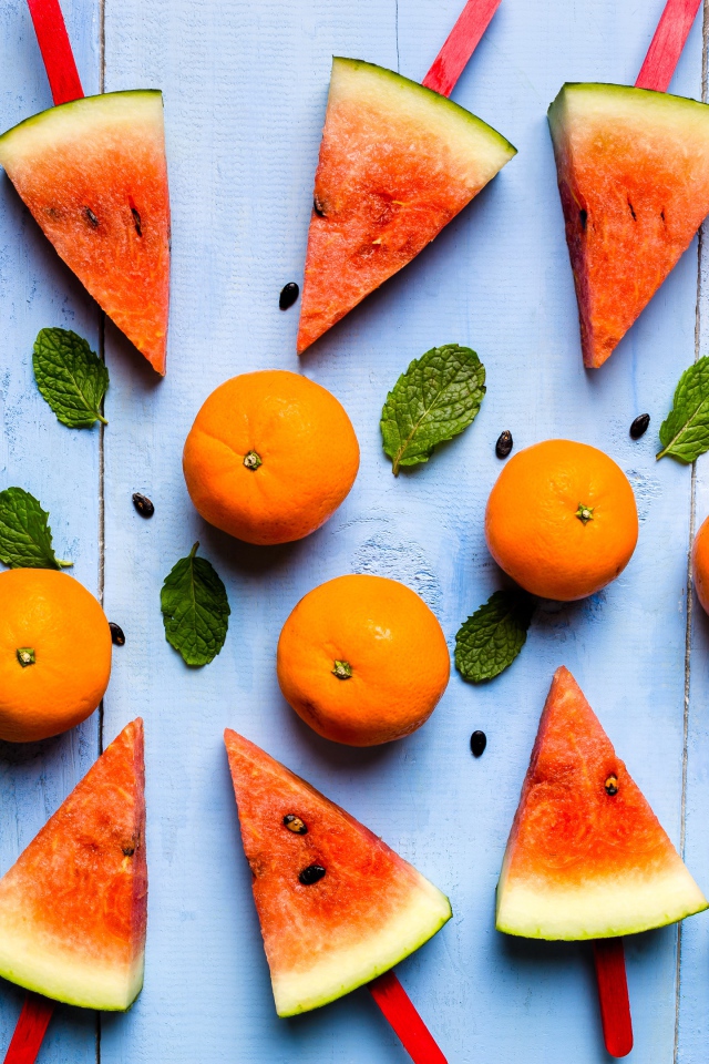 Кусочки арбуза на палочках на столе с мандаринами