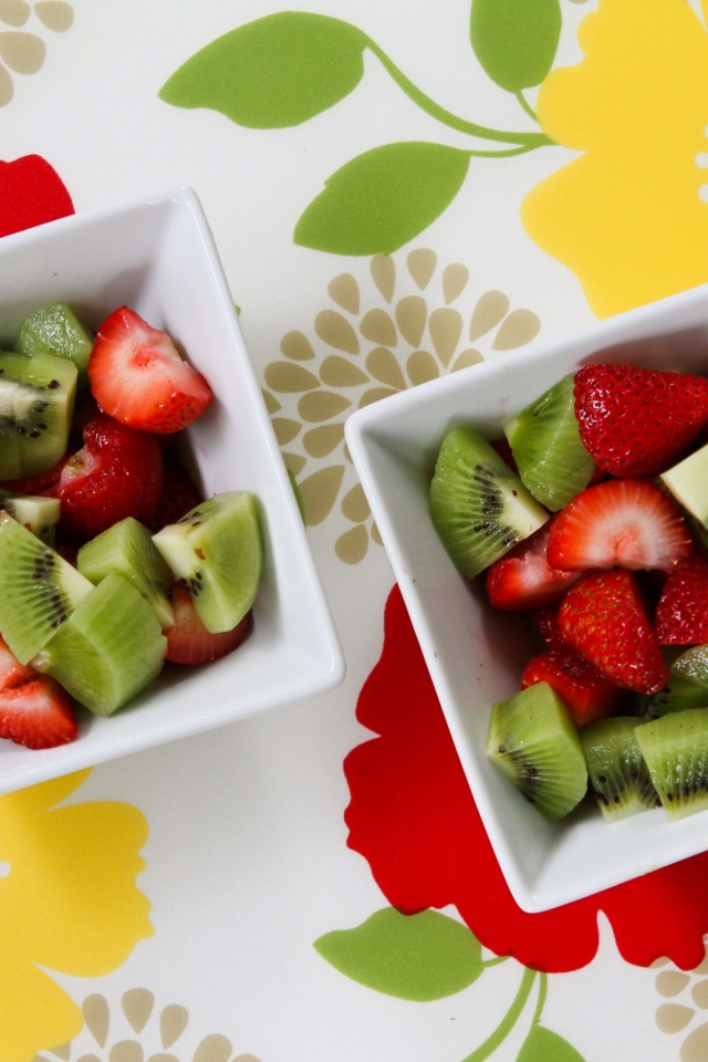 Салат с ягодами клубники и киви в белых тарелках на столе 