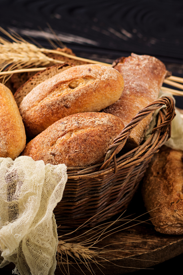 Свежая выпечка в корзине на столе с колосьями пшеницы