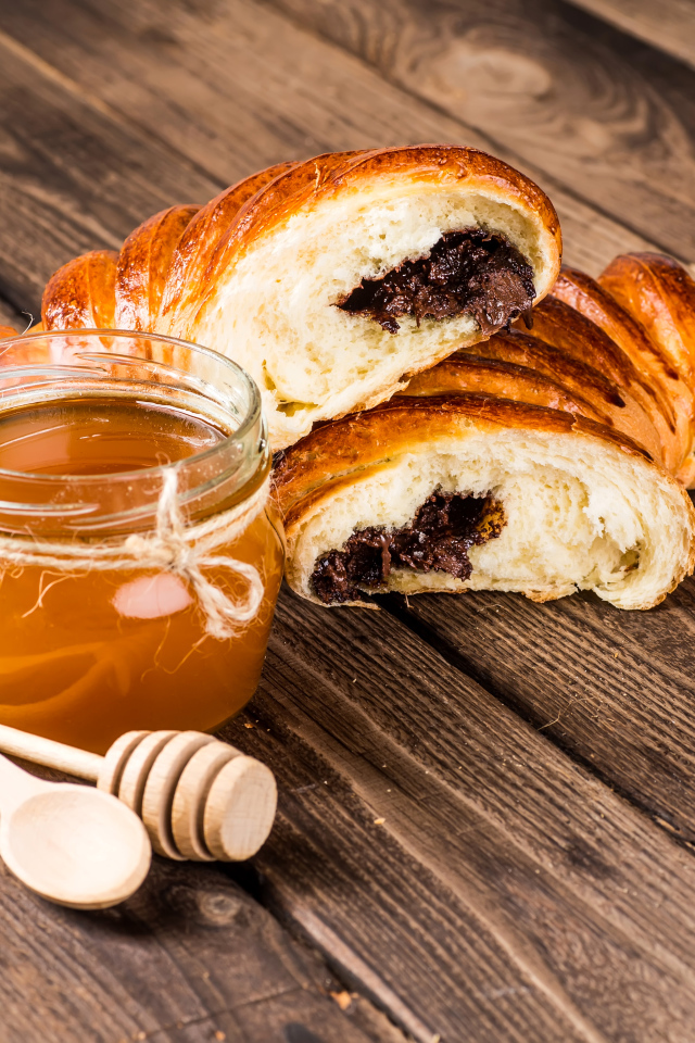 Банка меда, свежая выпечка и ложки на деревянном столе