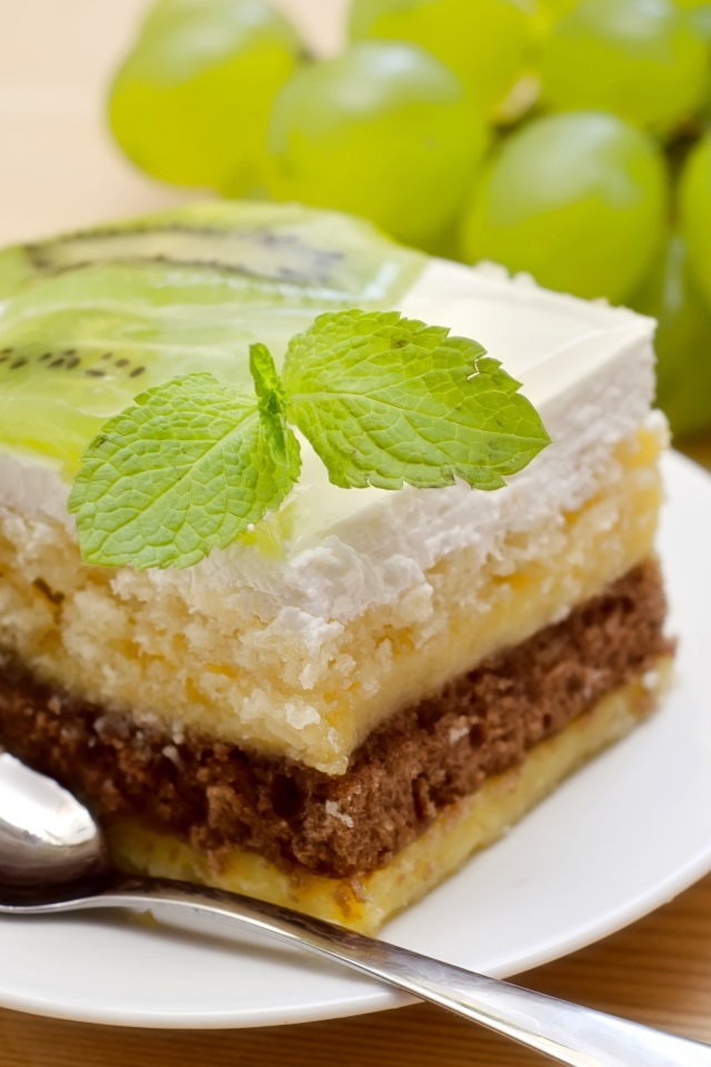 Кусок торта с киви и мятой на столе с виноградом