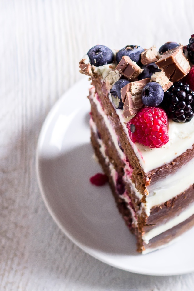 Кусок торта с ягодами малины и черники на блюдце