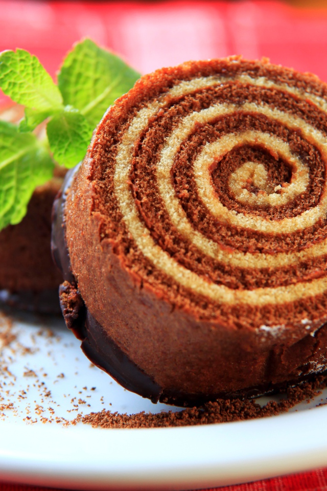 Кусок сладкого рулета с шоколадом и листом мяты на тарелке