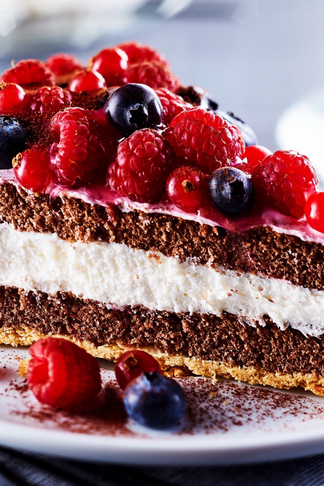 Аппетитный кусок торта на тарелке с ягодами малины, красной смородины и черники