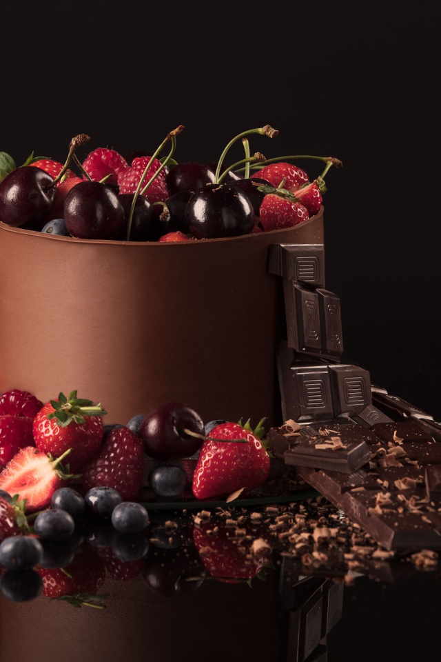 Черный шоколад с ягодами черники, малины, клубники и вишни на черном фоне