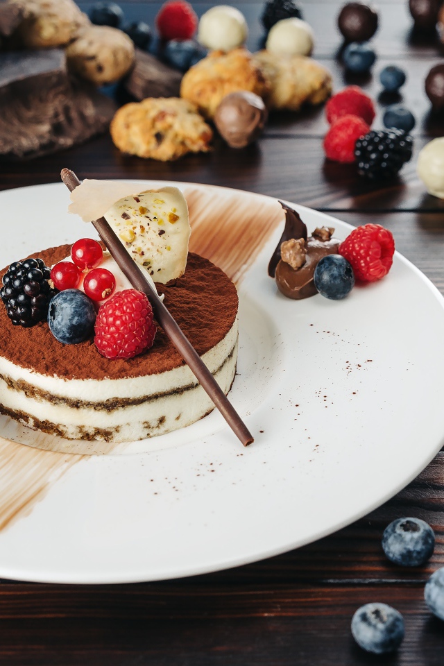 Пирожное с ягодами и шоколадом на белой тарелке 