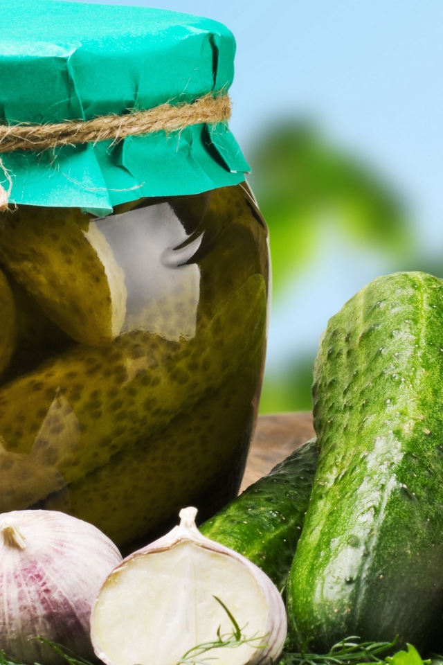 Консервированные огурцы в банке на столе со свежими огурцами и чесноком