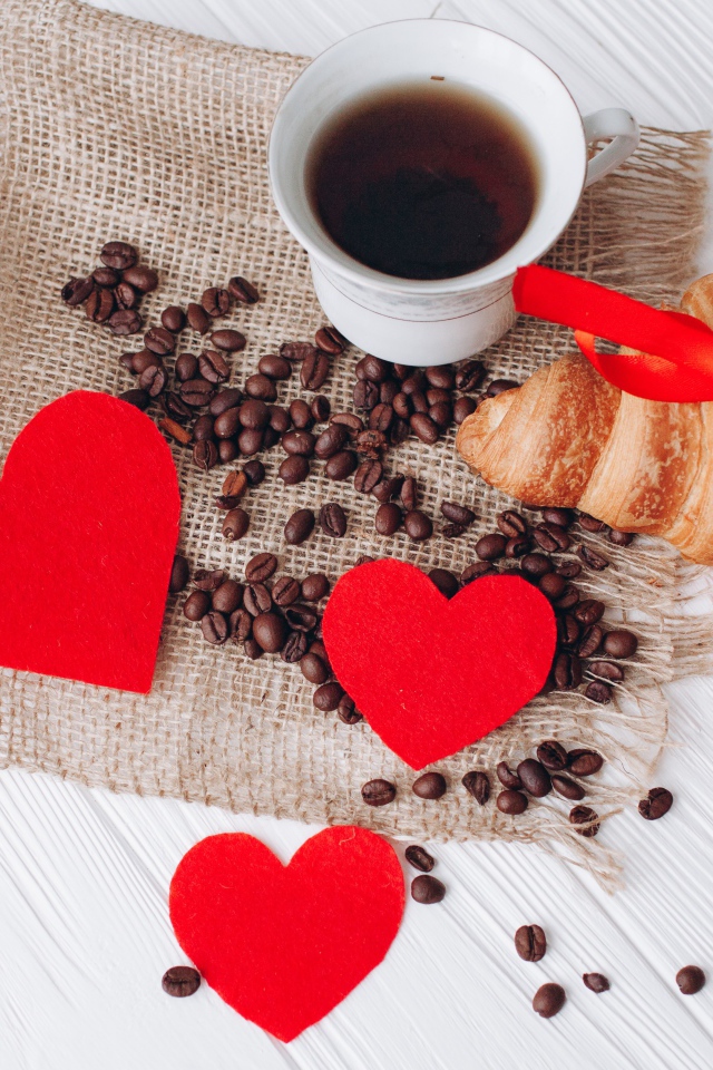 Круассан с чашкой кофе и кофейными зернами на столе с красными сердечками