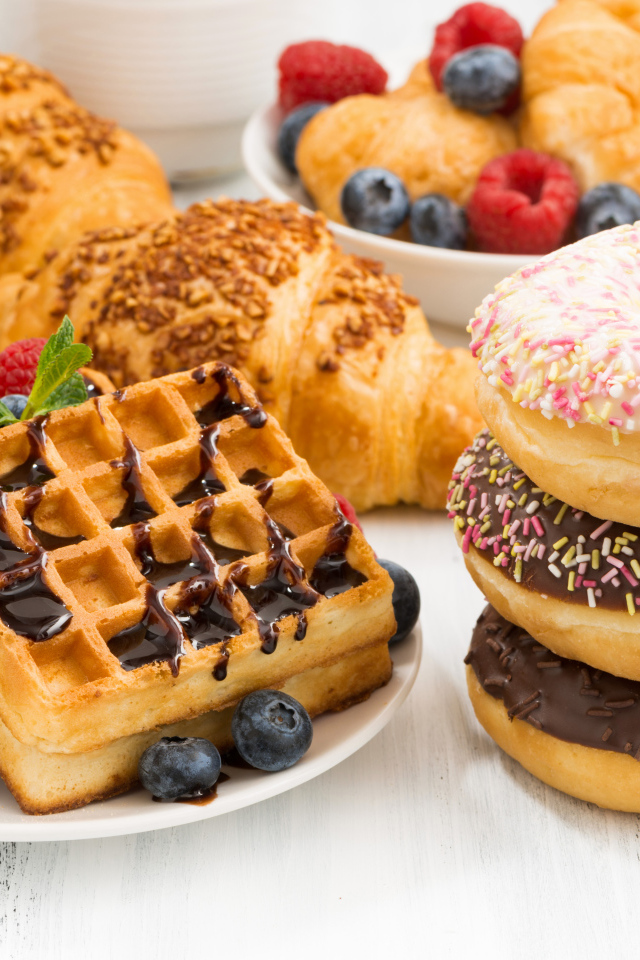 Круассаны, вафли и пончики на столе с ягодами