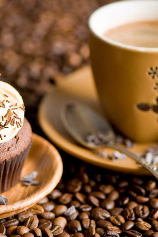 Кекс с кремом и чашкой кофе стоят на кофейных зернах 