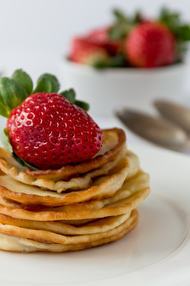 Оладьи с ягодами свежей клубники на белой тарелке 