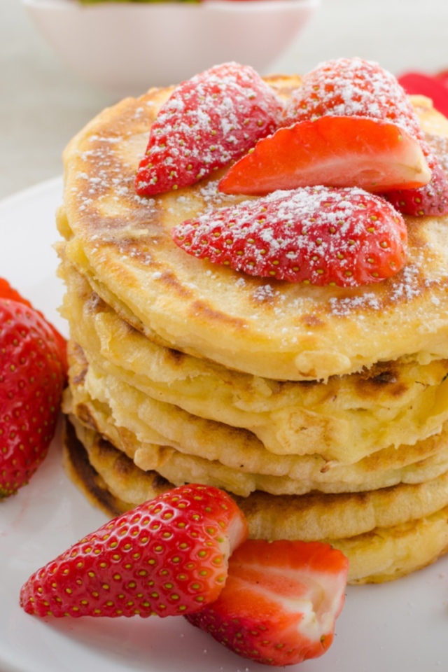 Оладьи с клубникой и сахарной пудрой на белой тарелке 