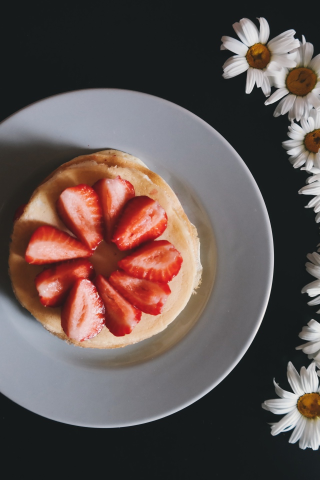 Оладьи с клубникой на тарелке на сером фоне с ромашками