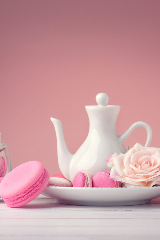 Розовый десерт макарун на столе с белый чайником и цветами розы
