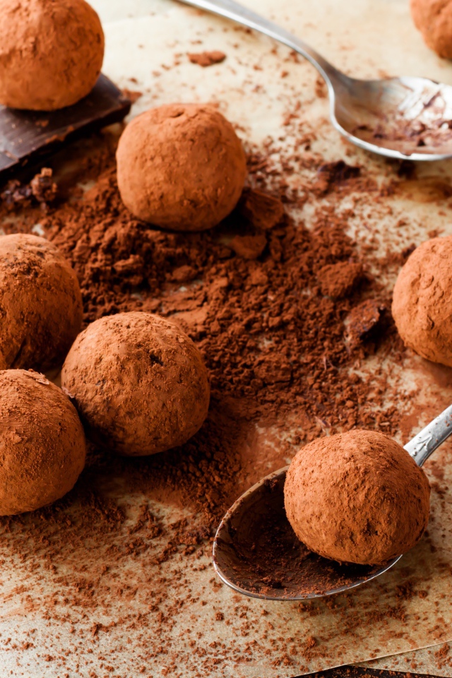 Круглые шоколадные конфеты в какао на столе с ложками