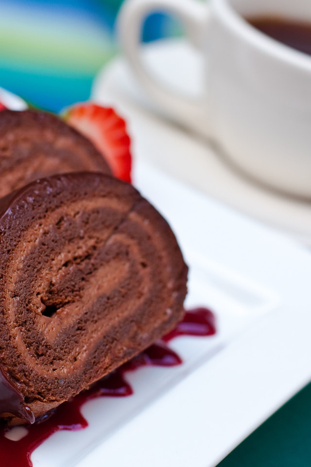 Сладкий рулет с клубничным джемом и чашкой чая на столе