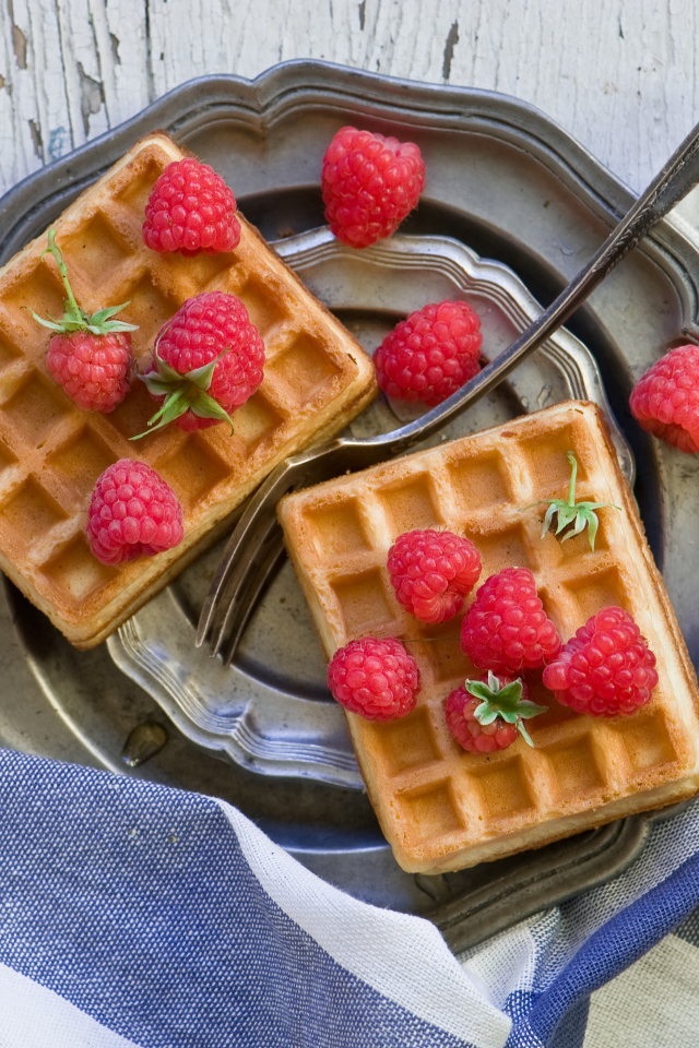 Сладкие вафли с ягодами малины на столе 