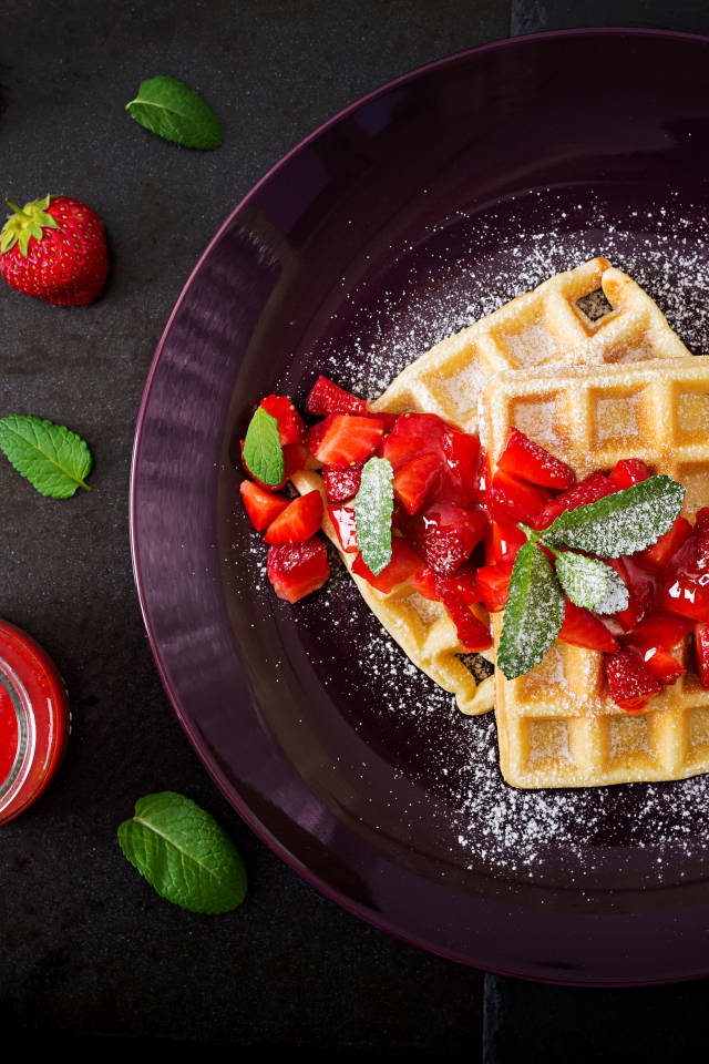 Сладкие вафли с клубникой и сахарной пудрой на тарелке 