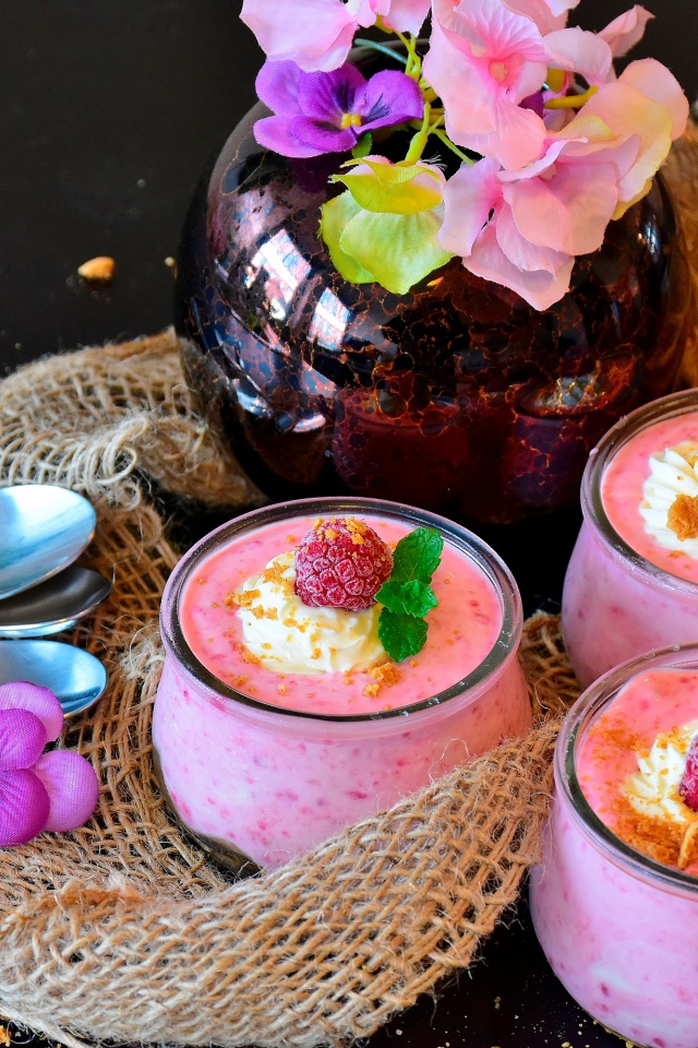 Три банки десерта с малиной на столе с цветами