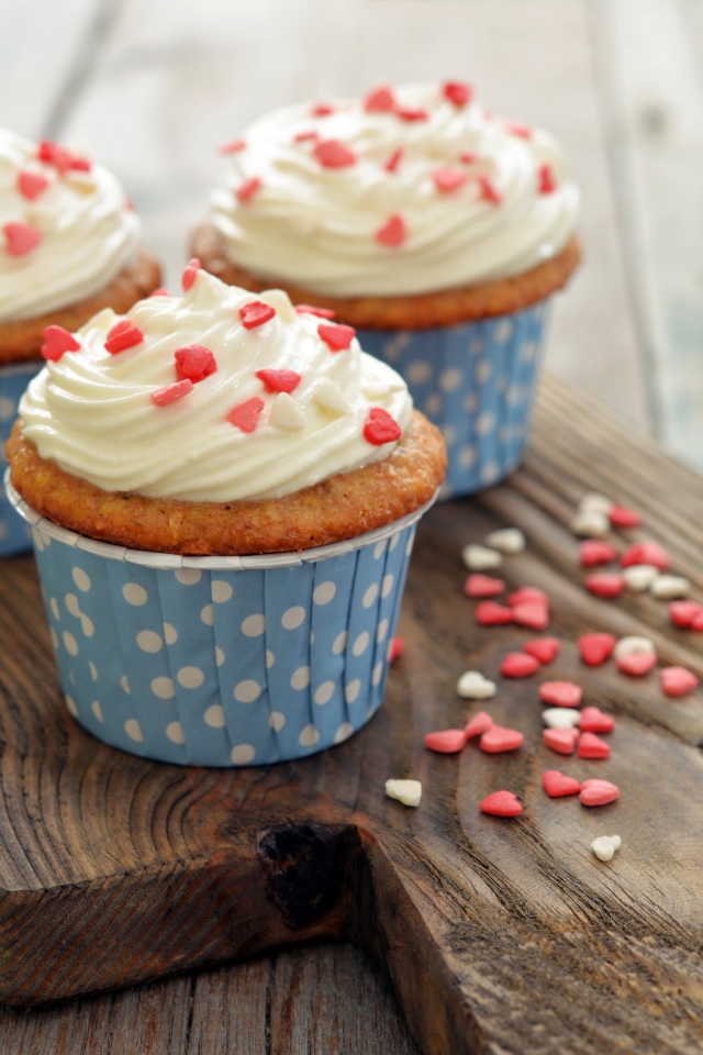 Три кекса со сливками украшены сердечками стоят на разделочной доске