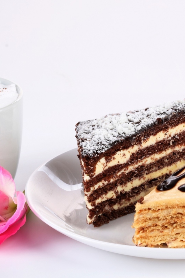 Два куска торта на столе с чашкой кофе и розовым цветком