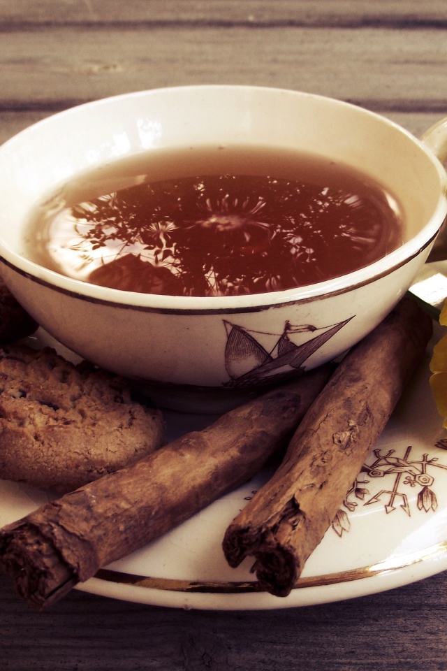 Чашка чая с печеньем, палочками корицы и цветами 