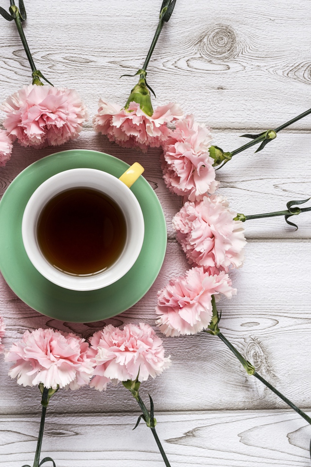 Чашка чая с розовыми гвоздиками на деревянном фоне