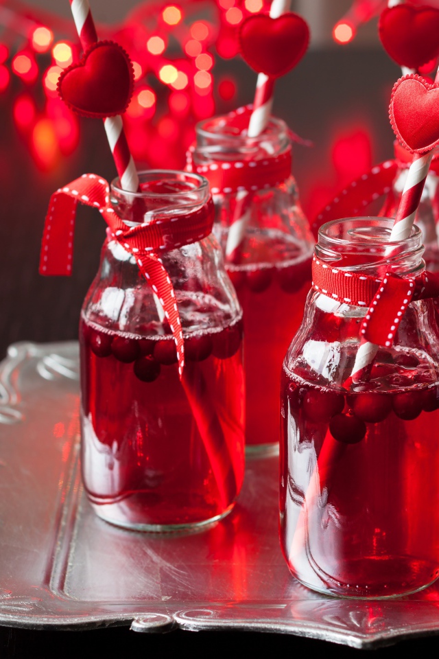 Вкусный напиток с клюквой в стеклянных бутылках на столе с трубочками