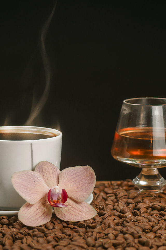Ароматная чашка кофе на столе с бокалом виски, кофейными зернами и цветком орхидеи