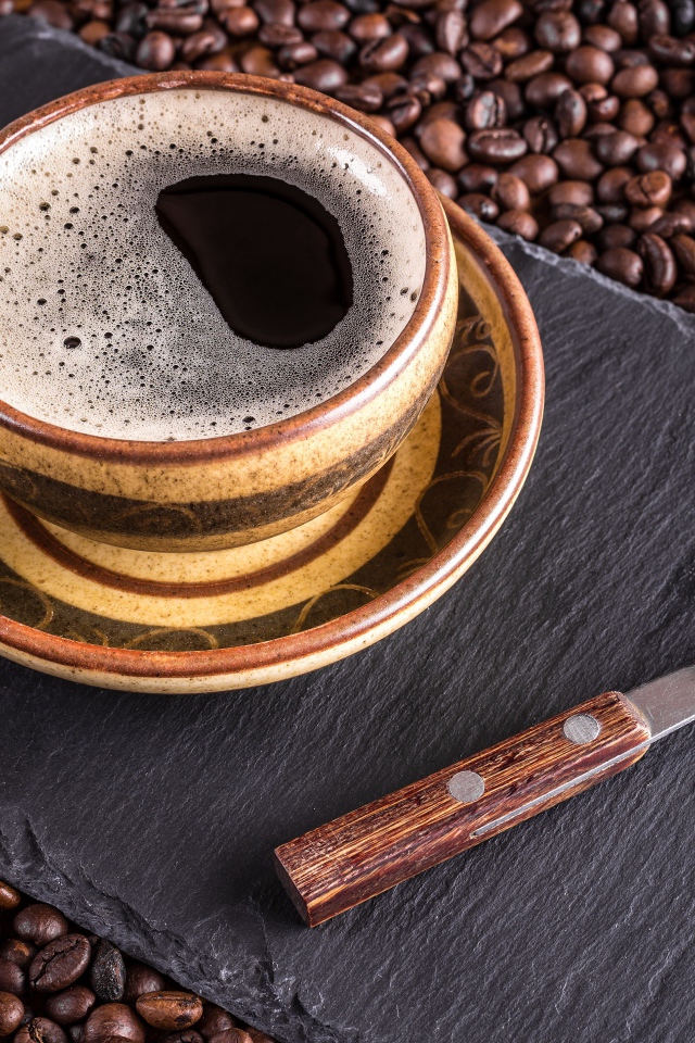 Большая чашка кофе с чайной ложкой стоят на кофейных зернах