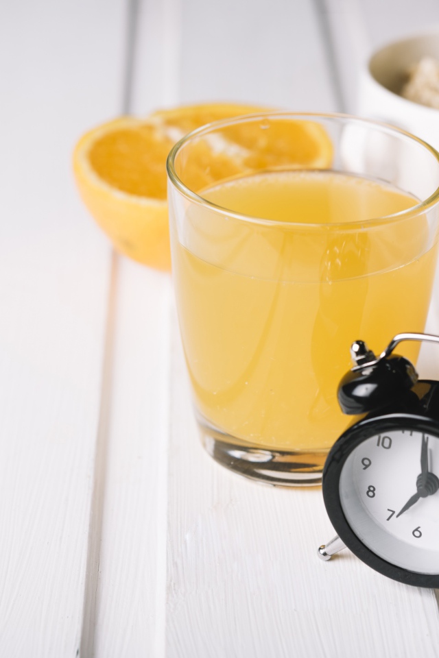 Черный будильник на столе со стаканом сока и хлопьями 