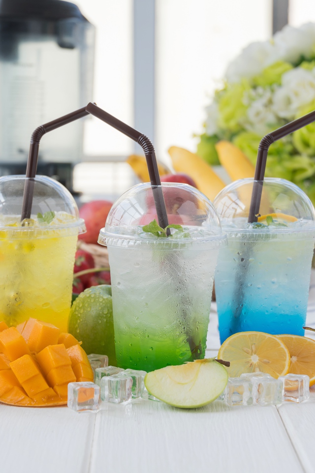 Коктейли в стаканах с трубочками на столе с кубиками льда и фруктами