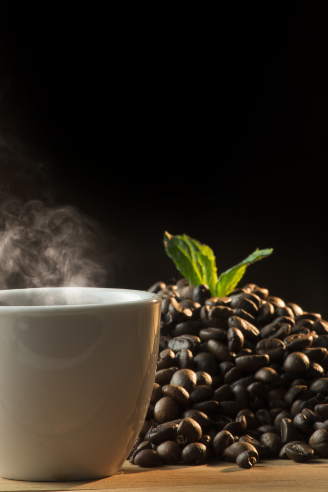 Кофейные зерна на столе с чашкой горячего кофе 
