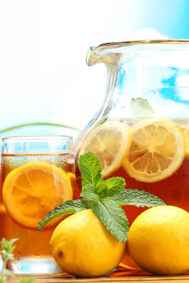 Холодный лимонад в графине на столе со стаканами и плодами лимона