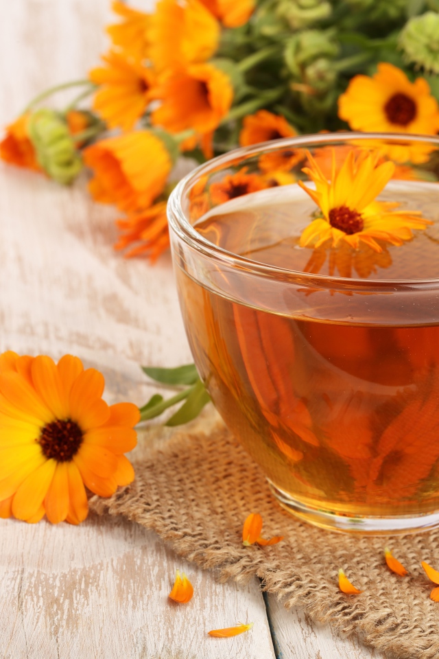Стеклянная чашка чая с цветками календулы на столе