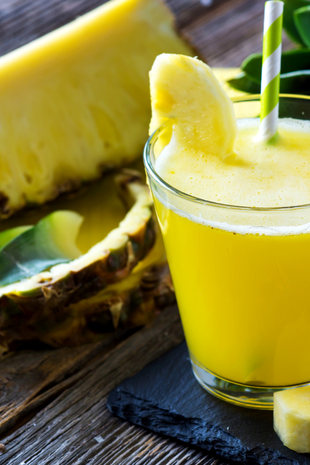 Ананасовый напиток в стакане на столе со свежими ананасами