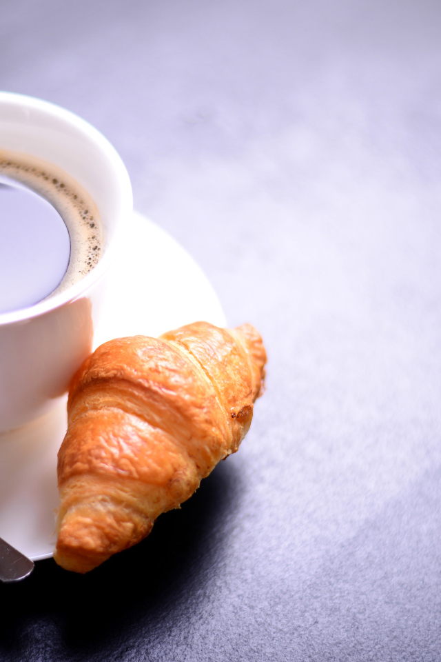 White cup of coffee on a table with a croissant