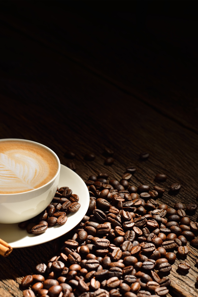 Белая чашка кофе с пенкой на столе с кофейными зернами и корицей